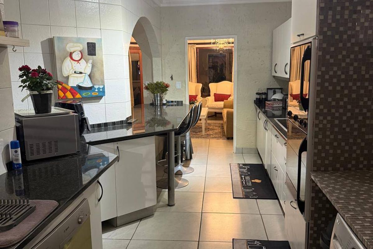 A functional kitchen featuring granite countertops, built-in cabinetry, an integrated oven, and a breakfast bar, leading through an archway to the living area.