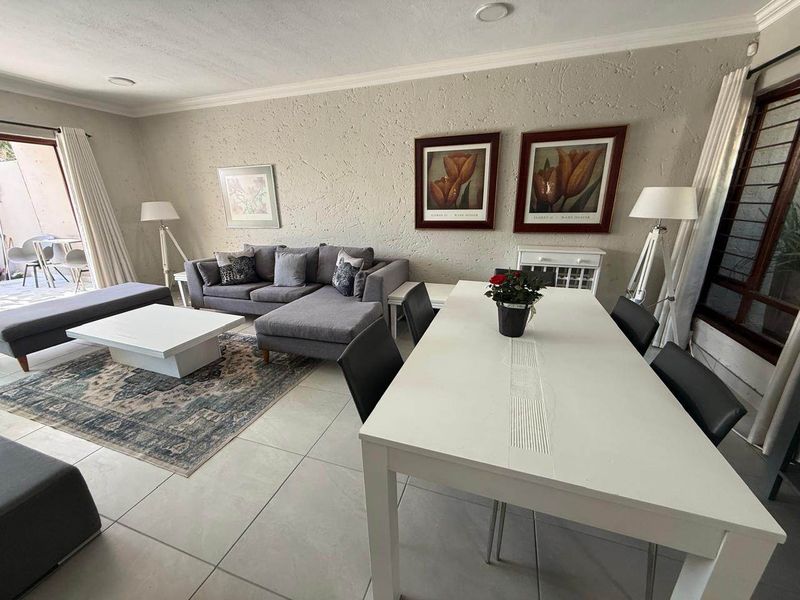 Spacious open-plan living and dining area featuring neutral tiled flooring, textured walls, and direct access to an outdoor patio through sliding glass doors.