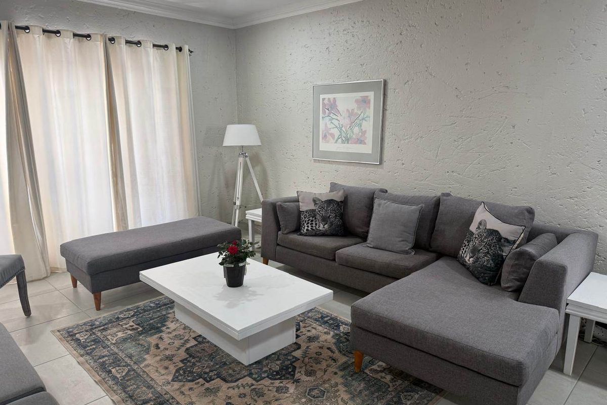 A well-maintained living room featuring neutral textured walls, tiled flooring, and a sliding glass door providing natural light.