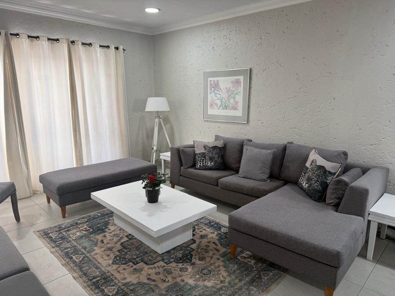 A well-maintained living room featuring neutral textured walls, tiled flooring, and a sliding glass door providing natural light.