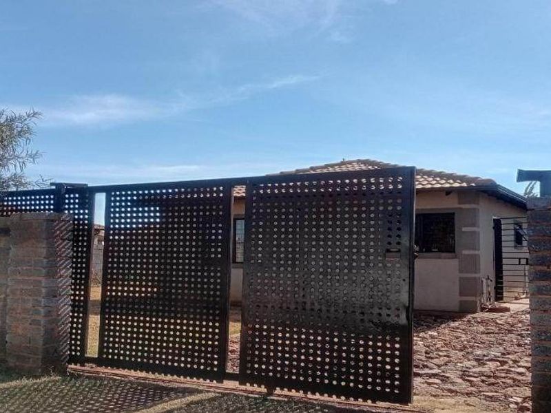 Front view of the property featuring a modern perforated metal sliding gate, brick boundary wall, and a tiled roof structure.