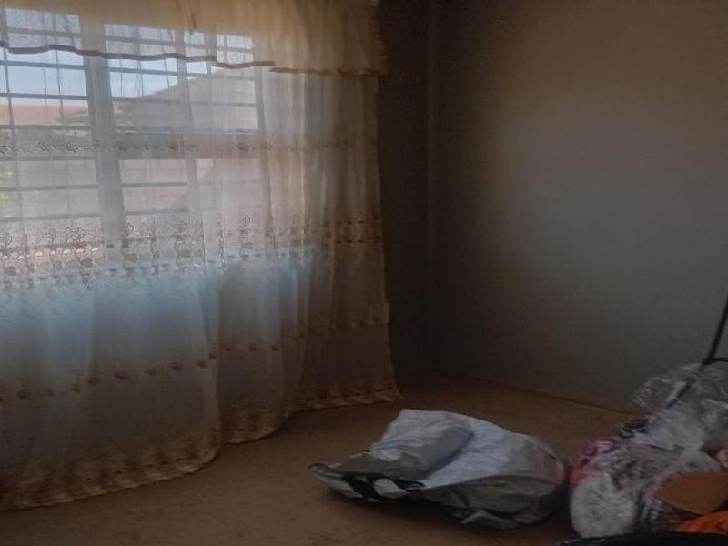 A sparsely furnished bedroom featuring a window with security bars and neutral wall finishes, offering a blank canvas for potential interior updates.