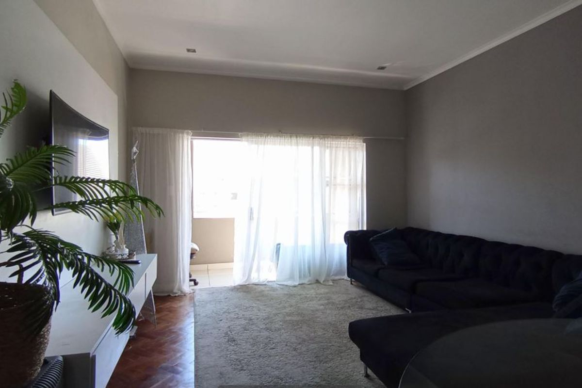 A well-maintained living room featuring classic parquet flooring, recessed lighting, and a large sliding glass door providing access to an outdoor balcony area.