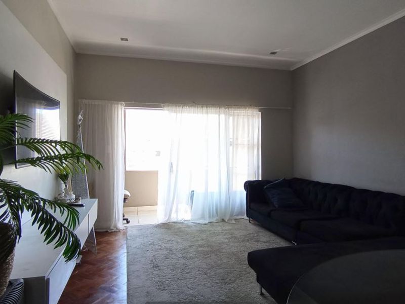 A well-maintained living room featuring classic parquet flooring, recessed lighting, and a large sliding glass door providing access to an outdoor balcony area.