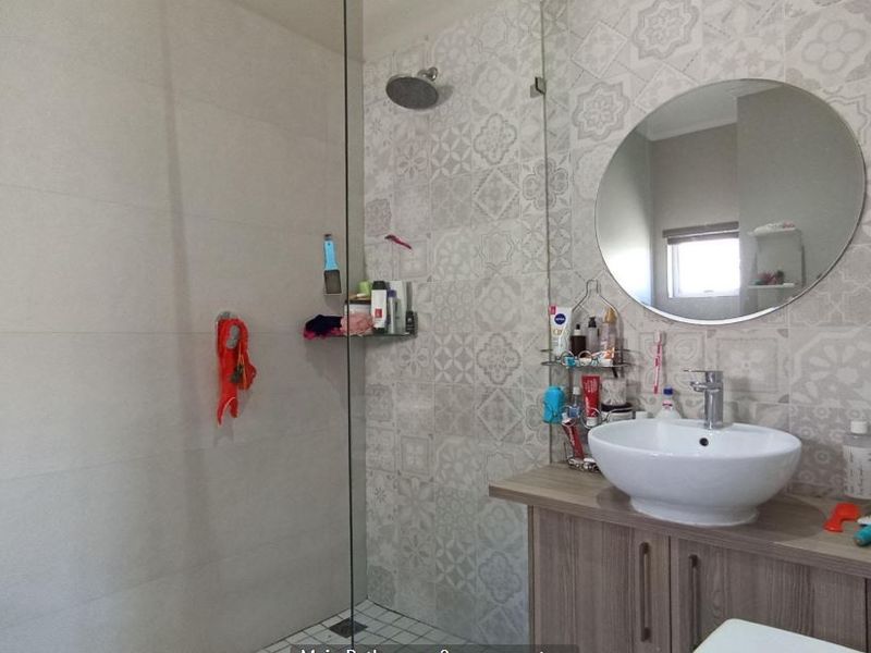 Modern bathroom featuring a walk-in shower with a glass screen, rain shower head, and a vanity unit with a vessel sink.