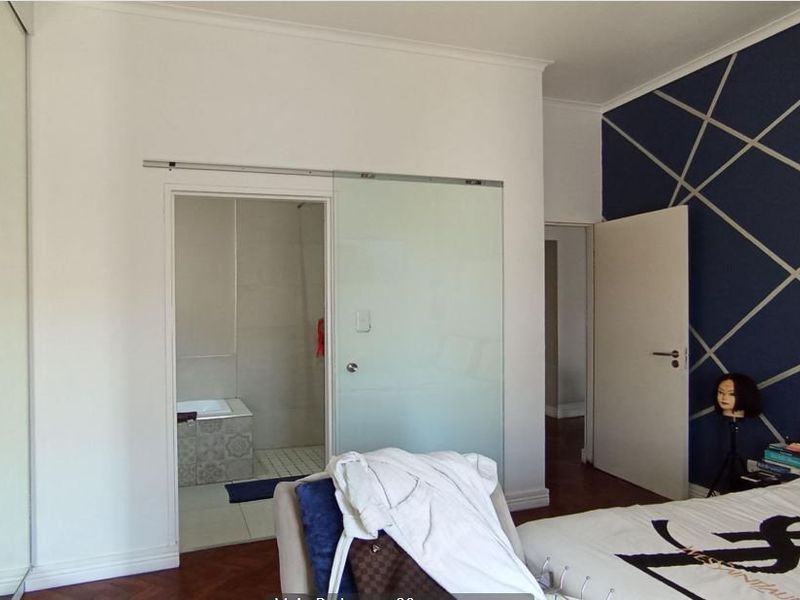 Bedroom featuring parquet flooring, built-in wardrobe, and a modern sliding glass door providing access to an en-suite bathroom.