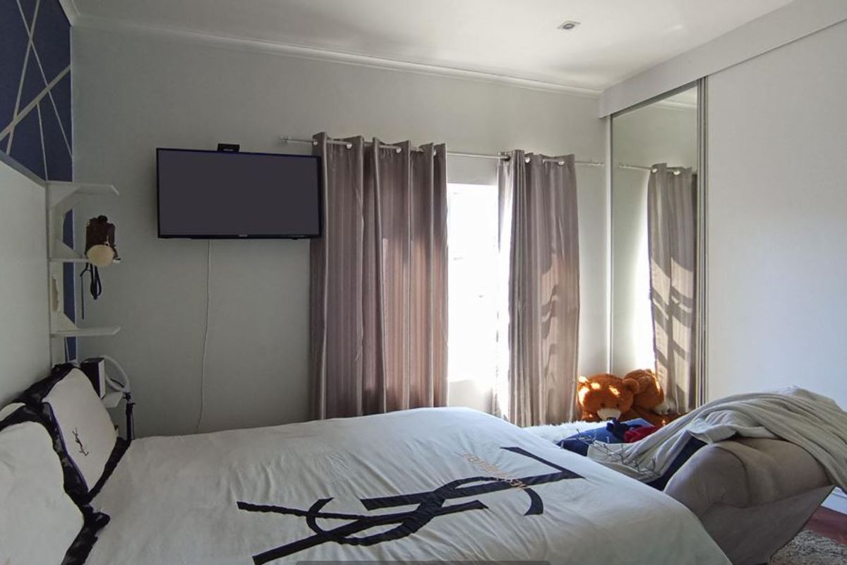 A well-lit bedroom featuring built-in sliding door wardrobes with mirrored panels and recessed ceiling lighting.