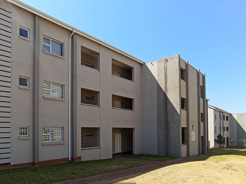 Exterior view of a multi-story apartment complex featuring balconies, paved walkways, and standard window configurations with security bars.