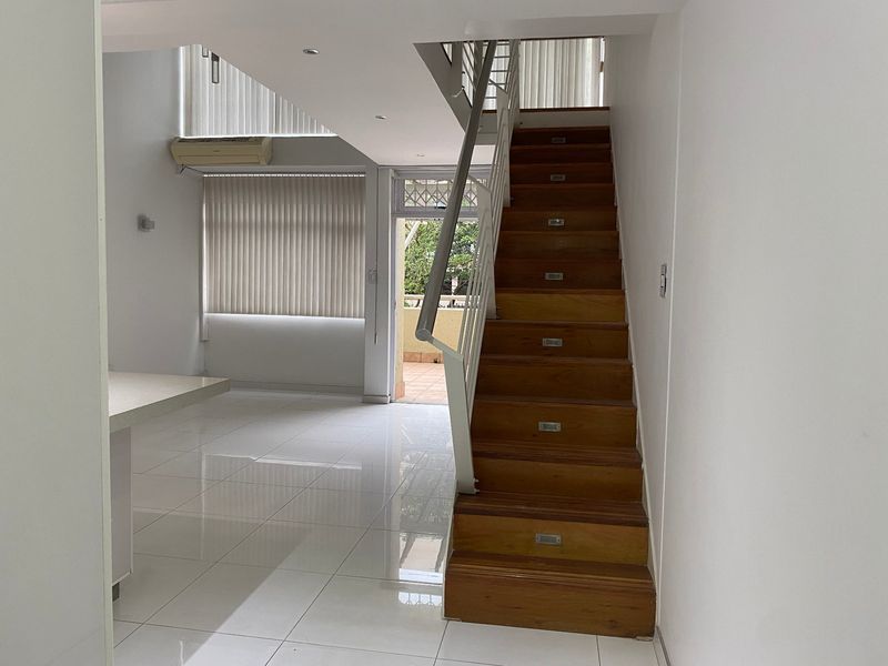 Open plan living area featuring a wooden staircase with integrated lighting, tiled flooring, and access to an outdoor patio area.