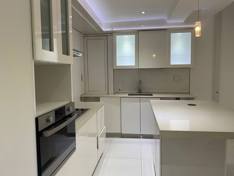 Modern kitchen featuring high-gloss cabinetry, quartz countertops, a central island, built-in oven, electric hob, and integrated lighting.