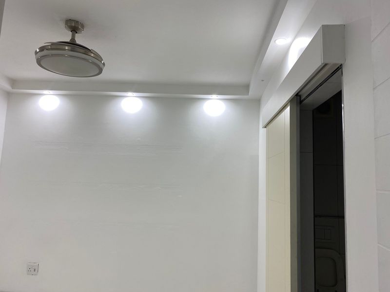 A minimalist bedroom interior featuring recessed ceiling lighting, a modern ceiling fan, and a sliding door leading to an adjacent space.