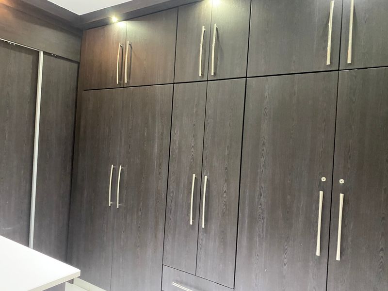A bedroom featuring extensive dark wood-grain built-in cupboards with modern metal handles and integrated recessed lighting.
