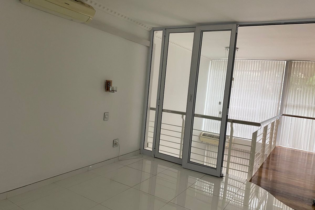Bright and spacious living area featuring polished tile flooring, a wall-mounted air conditioning unit, and sliding glass doors leading to an adjacent balcony space.