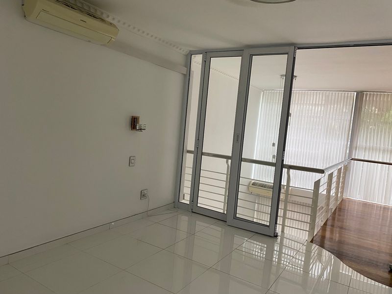 Bright and spacious living area featuring polished tile flooring, a wall-mounted air conditioning unit, and sliding glass doors leading to an adjacent balcony space.