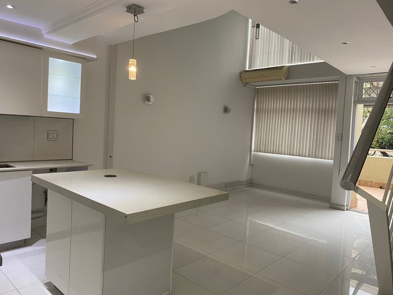 Modern open-plan living area featuring a sleek kitchen island, tiled flooring, and neutral finishes, offering a bright and versatile space for living and dining.