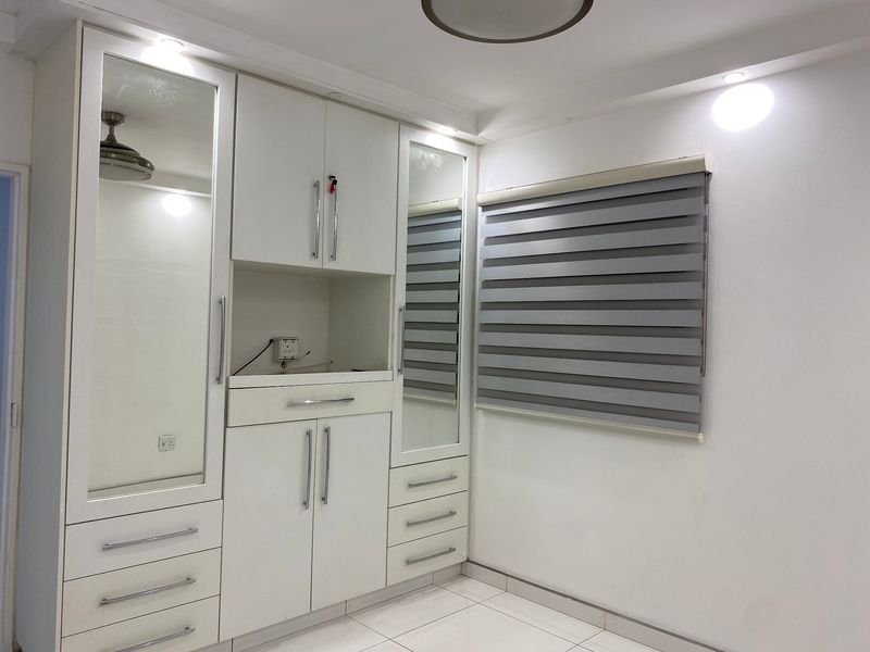 A clean, modern bedroom featuring extensive white built-in cabinetry with integrated mirrors, sleek hardware, and contemporary roller blinds.
