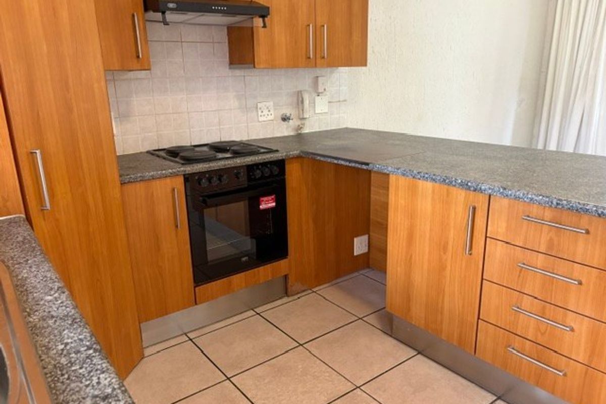 A functional kitchen featuring wood-look laminate cabinetry, granite-style countertops, built-in oven and hob, and tiled flooring.
