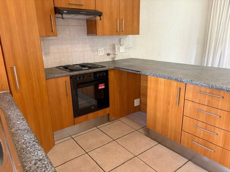A functional kitchen featuring wood-look laminate cabinetry, granite-style countertops, built-in oven and hob, and tiled flooring.