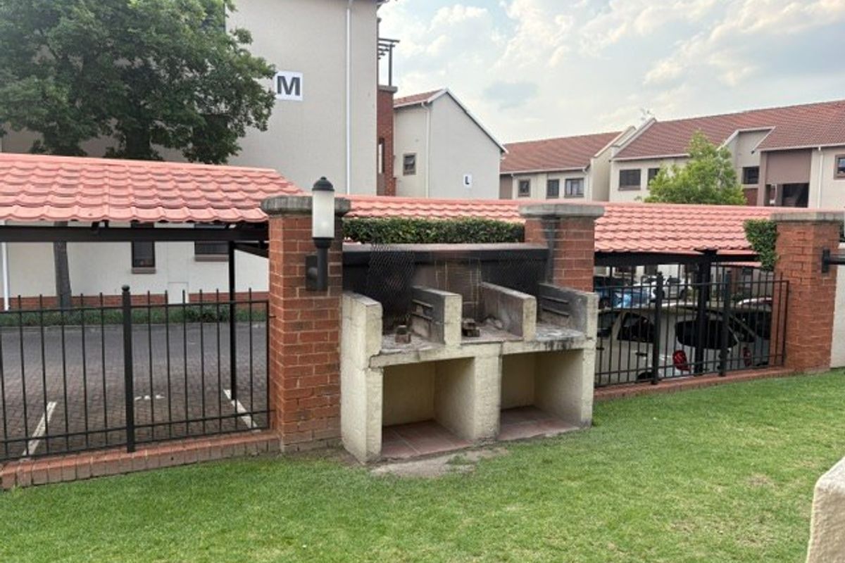 Communal outdoor area featuring a built-in brick braai, wrought iron fencing, and covered parking bays within the apartment complex.