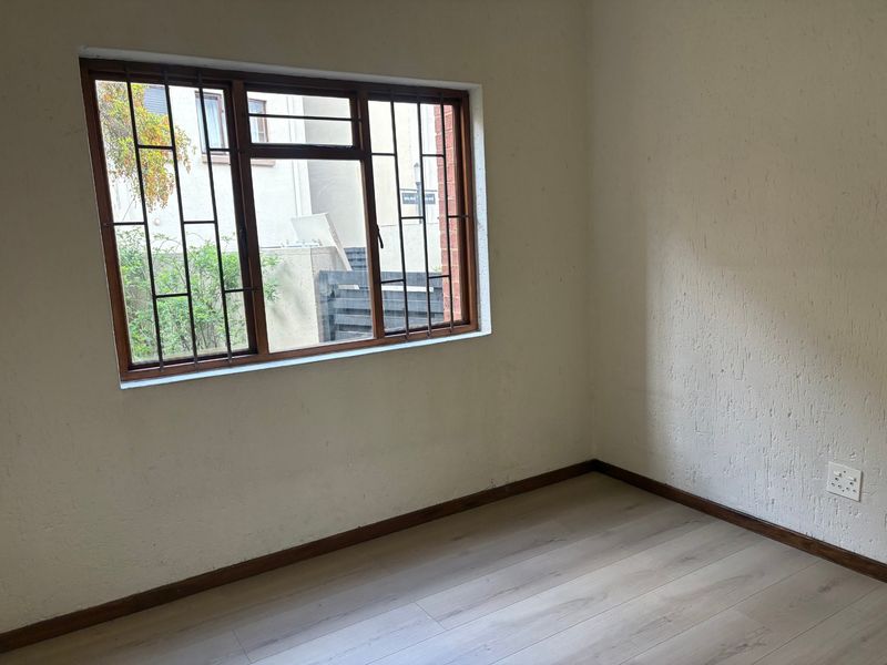 An empty bedroom featuring laminate flooring, a timber-framed window with security bars, and textured wall finishes.