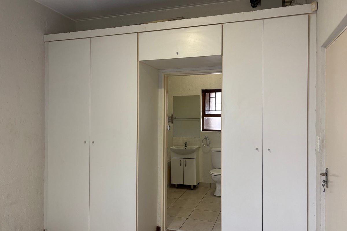 A bedroom featuring built-in cupboards with direct access to an en-suite bathroom, offering a functional layout ready for modernization.