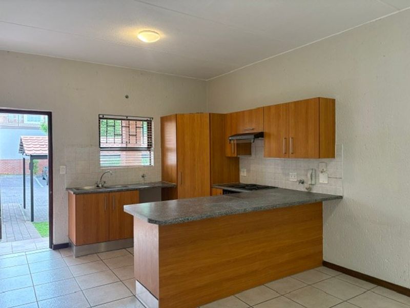 Functional kitchen featuring wood-look cabinetry, granite-style countertops, tiled flooring, and direct access to the exterior through a secure door.