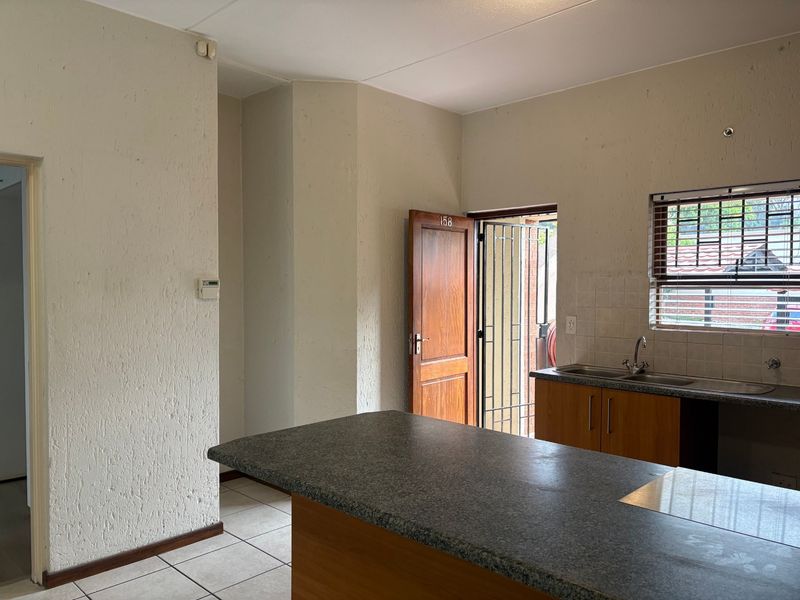 An empty kitchen featuring a granite-topped island, tiled flooring, and direct access to an exterior security gate.