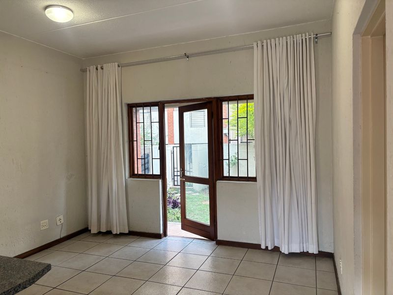 An empty living area featuring tiled flooring, security bars on windows, and a timber door leading to an outdoor space.