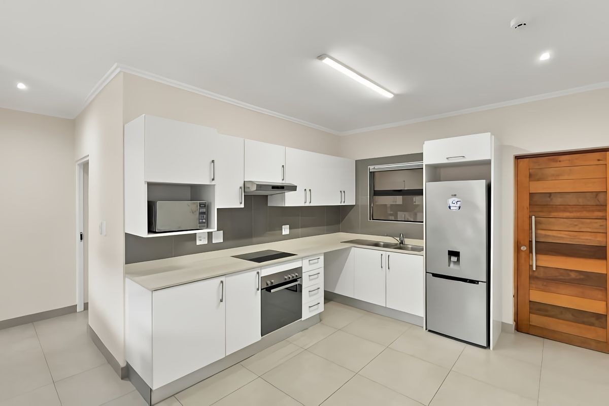 Modern kitchen featuring white cabinetry, stone-look countertops, integrated appliances, tiled backsplash, and neutral floor tiles in a clean, well-maintained space.