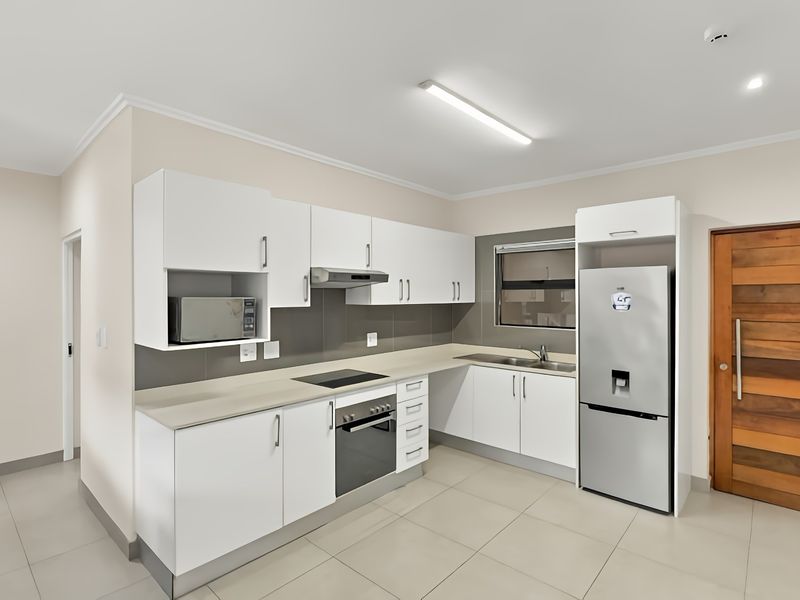 Modern kitchen featuring white cabinetry, stone-look countertops, integrated appliances, tiled backsplash, and neutral floor tiles in a clean, well-maintained space.