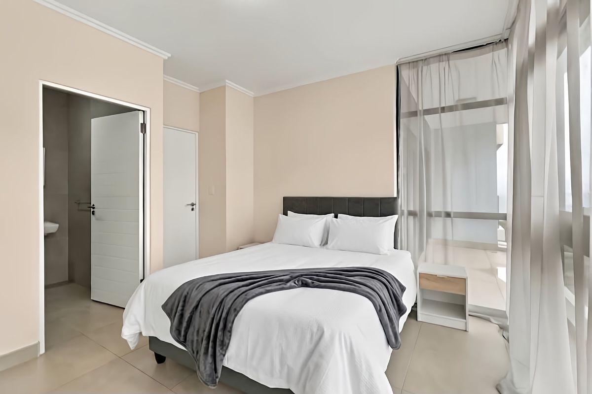 A well-maintained bedroom featuring neutral walls, tiled flooring, and direct access to an adjoining balcony through a large sliding glass door.