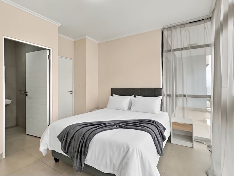 A well-maintained bedroom featuring neutral walls, tiled flooring, and direct access to an adjoining balcony through a large sliding glass door.