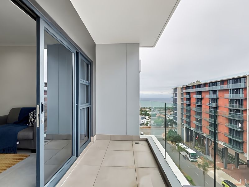 A modern, covered balcony featuring tiled flooring, a sleek glass balustrade, and sliding door access to the interior living space.