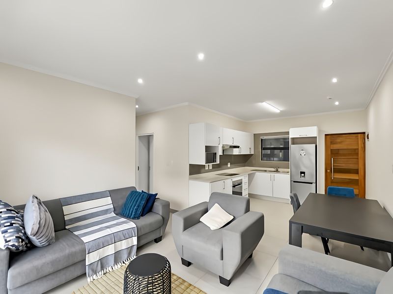 Modern open-plan living area featuring a well-appointed kitchen with built-in cabinetry, integrated appliances, and sleek tiled flooring throughout the space.