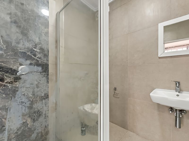Modern bathroom featuring a wall-mounted basin with chrome fixtures, a glass shower enclosure, and a combination of marble-effect and neutral beige wall tiling.