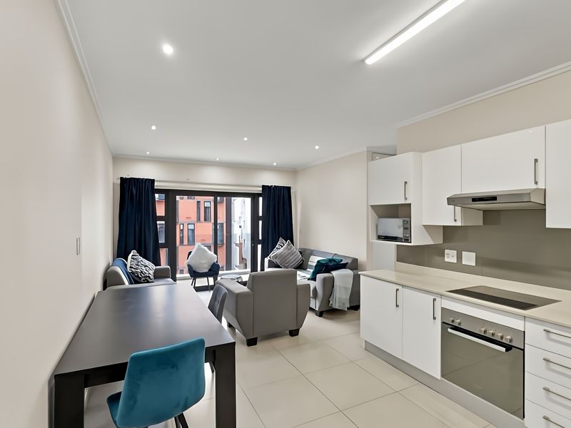 Modern open-plan living area featuring a sleek kitchen with built-in appliances, tiled flooring, and direct access to a balcony through sliding glass doors.