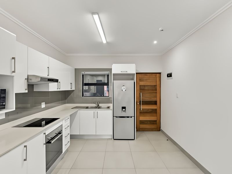 Modern kitchen featuring white cabinetry, stone countertops, integrated appliances, and tiled flooring, providing a clean and functional workspace.
