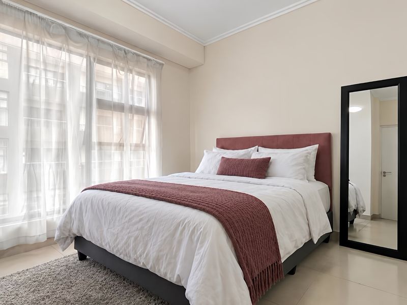 A bright and well-maintained bedroom featuring large windows with natural light, neutral wall finishes, and tiled flooring.