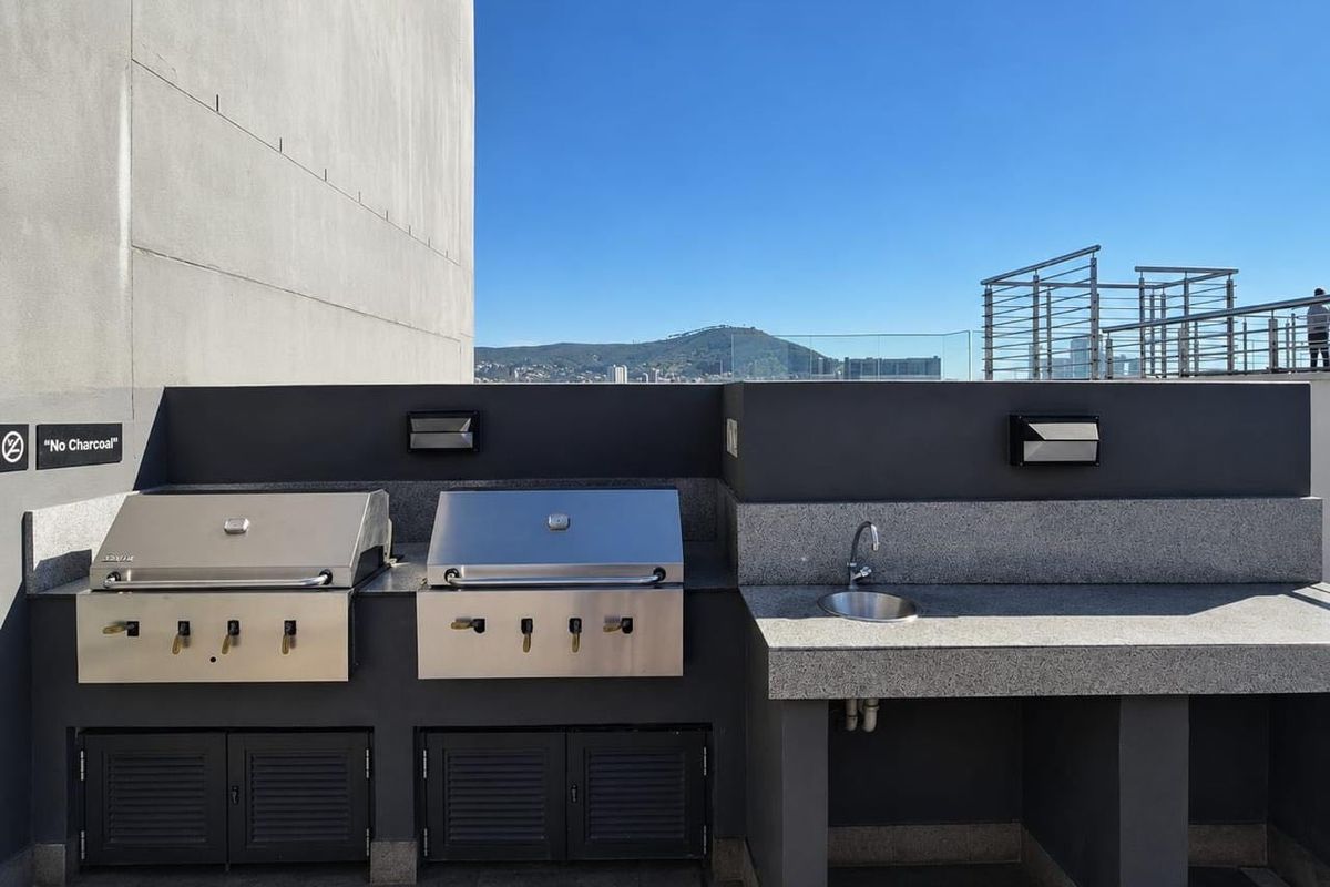 Outdoor entertainment area featuring built-in stainless steel gas grills, granite prep surfaces, and a sink, set against a backdrop of mountain views.