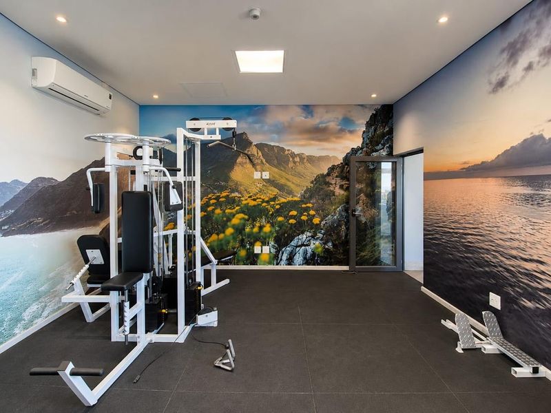 A well-maintained gym facility featuring tiled flooring, recessed lighting, a split-system air conditioner, and decorative landscape wall murals.