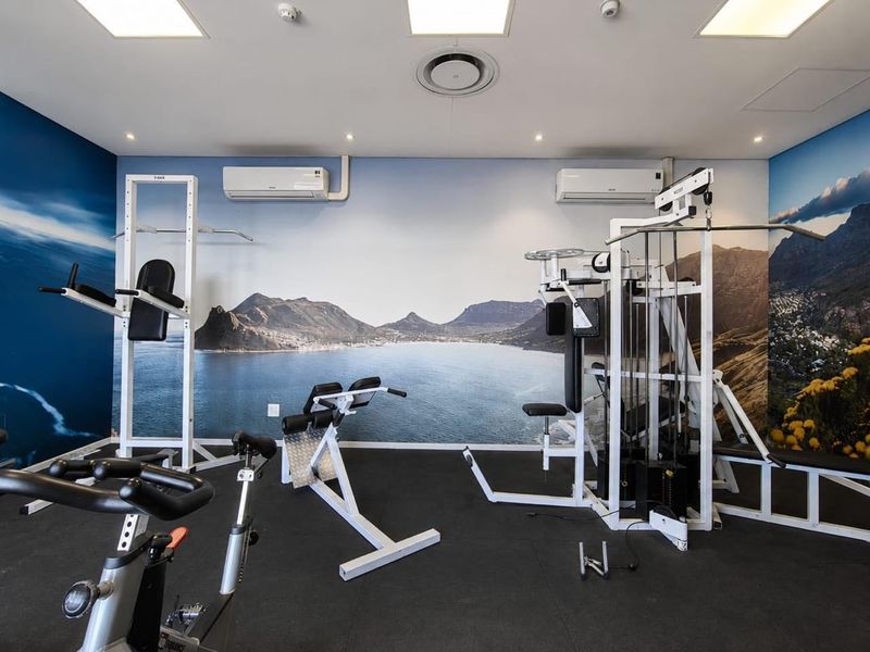 A well-maintained residential gym facility featuring rubber flooring, dual air conditioning units, and recessed lighting, equipped with various fixed strength training stations.
