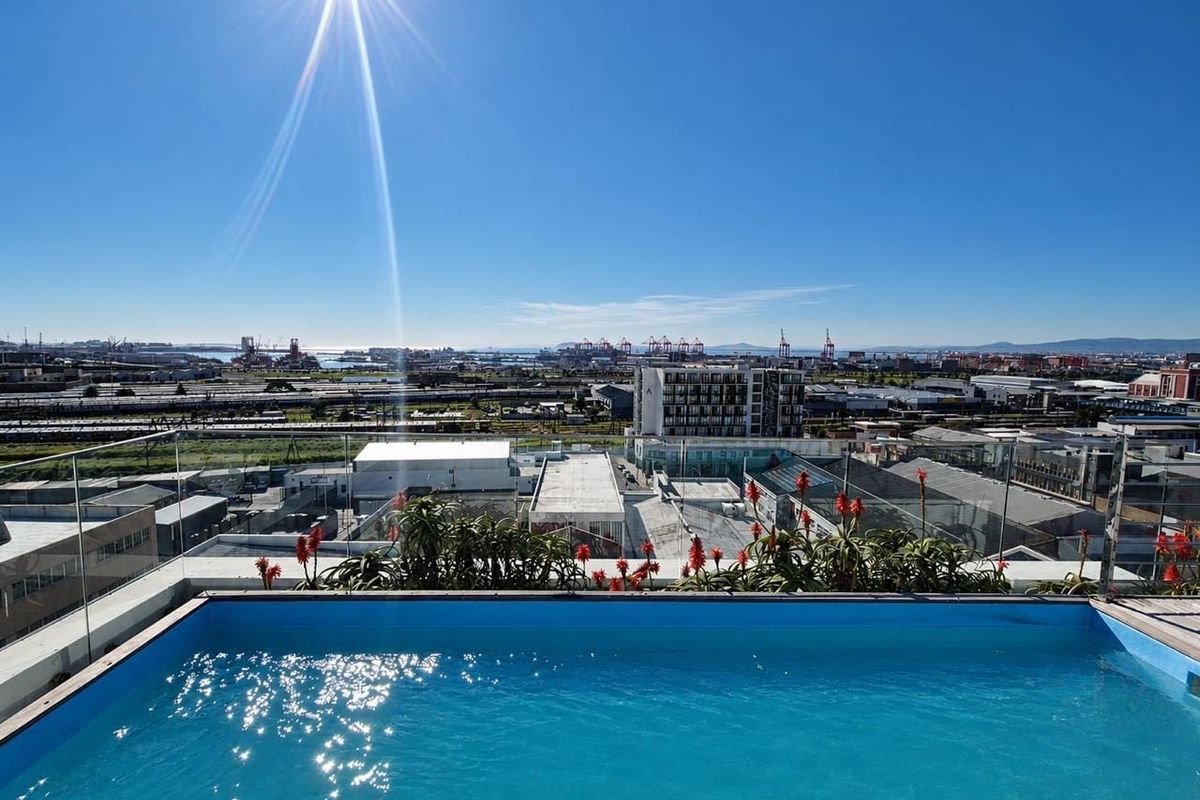 A rooftop swimming pool featuring a clear glass balustrade and panoramic urban and harbour views.