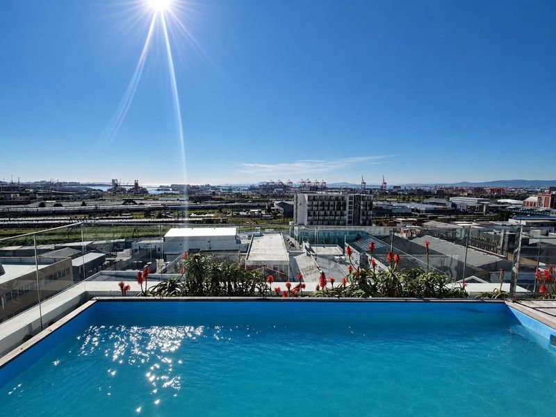 A rooftop swimming pool featuring a clear glass balustrade and panoramic urban and harbour views.