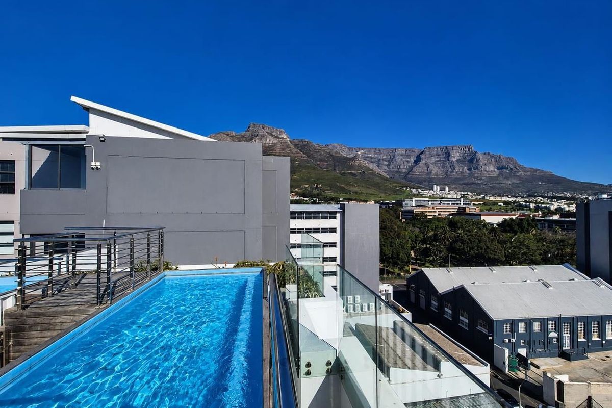 A rooftop swimming pool featuring a glass balustrade and timber decking, offering panoramic views of the mountain and surrounding cityscape.