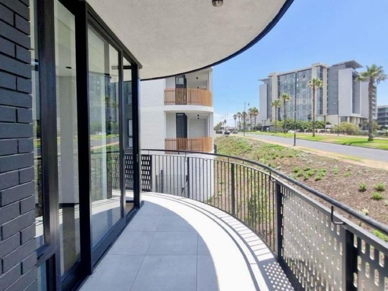 A modern, curved balcony featuring tiled flooring, metal railings, and large sliding glass doors, offering an elevated view of the surrounding urban landscape.