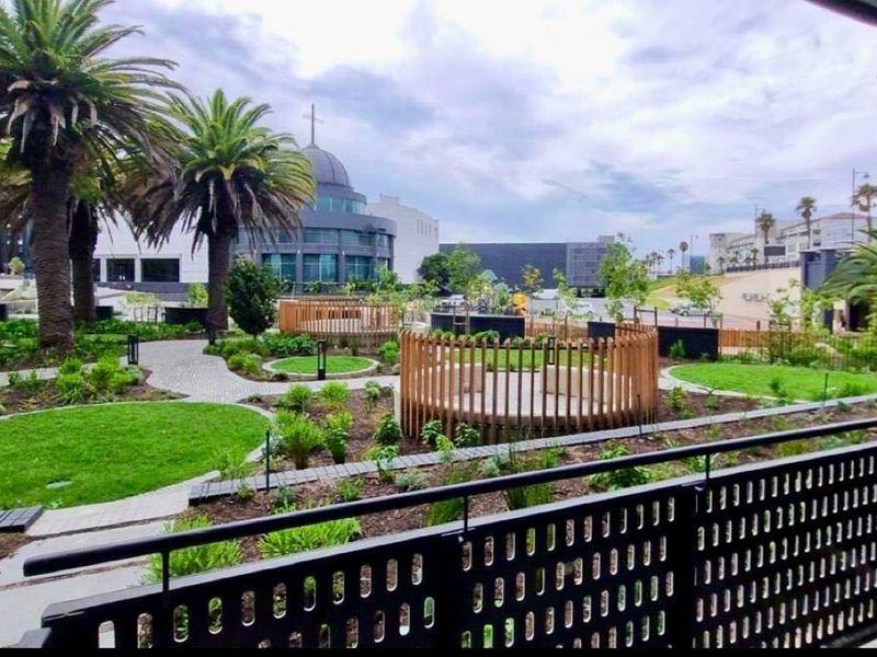 A view from a balcony overlooking a well-maintained landscaped garden area with paved paths and circular wooden seating features.