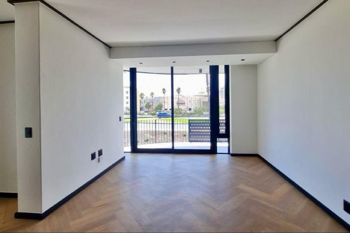 A bright, empty living area featuring high-quality herringbone timber flooring, modern black trim accents, and large sliding glass doors leading to a balcony.
