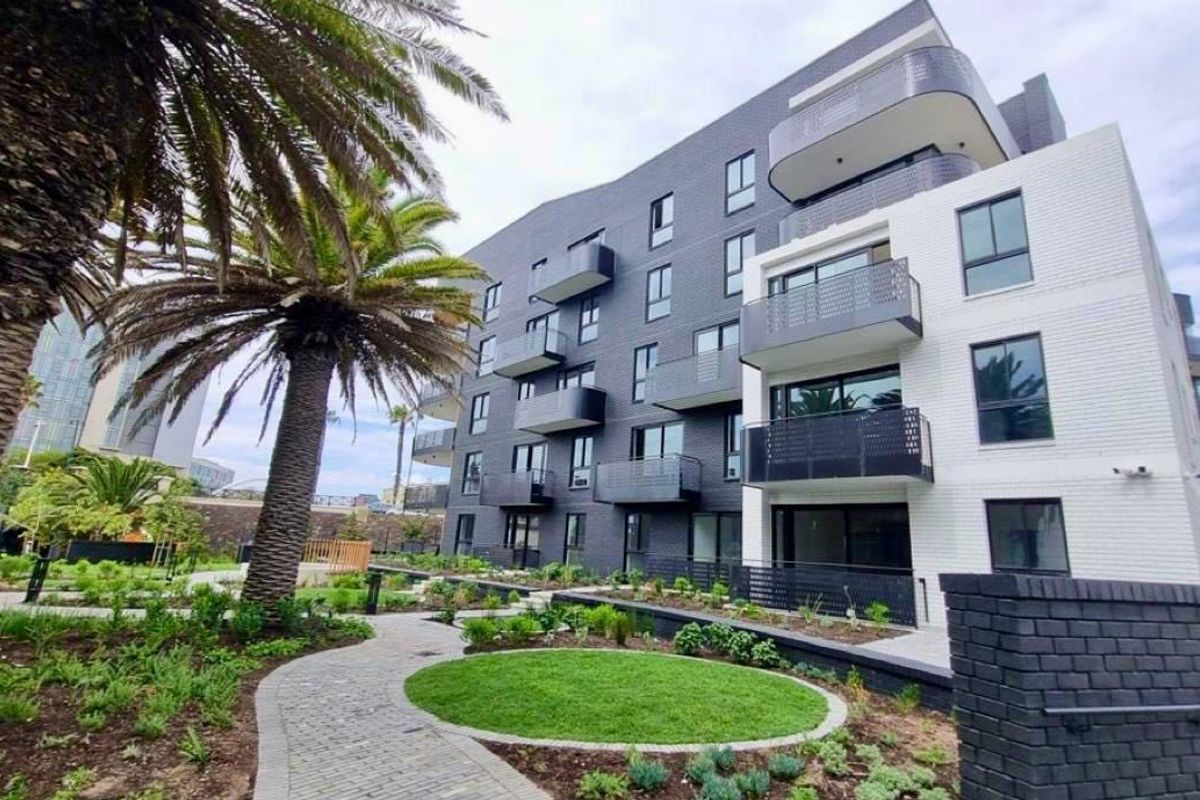 Modern apartment building exterior featuring a landscaped garden, paved pathways, and private balconies with contemporary brick and glass finishes.