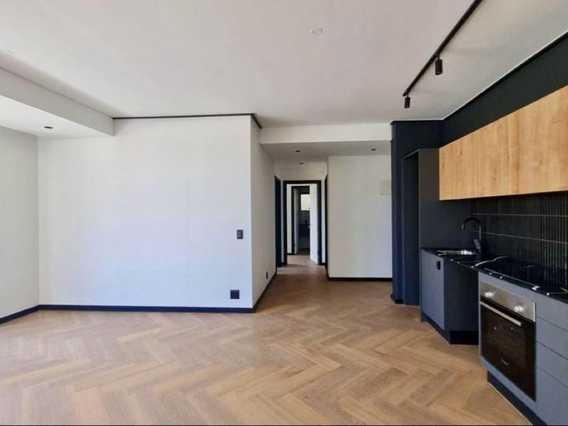 Modern open-plan living area featuring herringbone timber flooring, sleek dark cabinetry, integrated kitchen appliances, and floor-to-ceiling windows providing ample natural light.