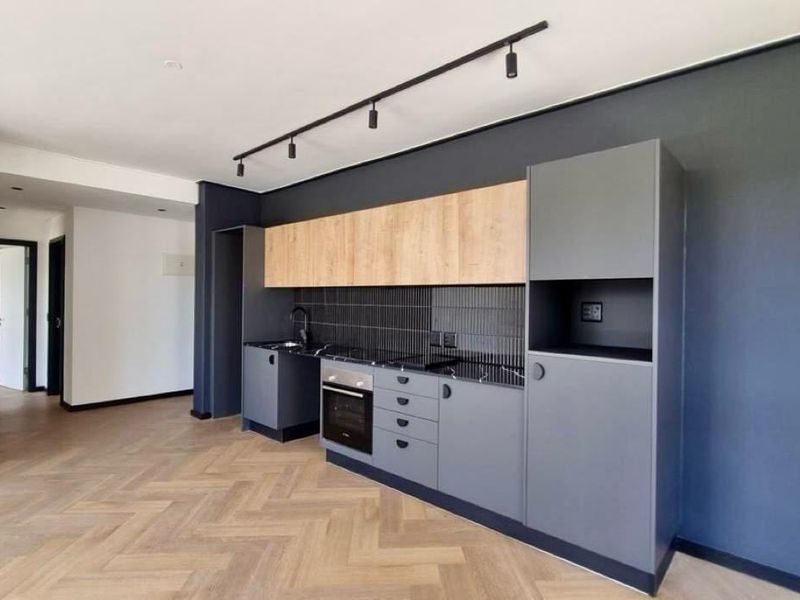 Modern kitchen featuring sleek grey and wood-tone cabinetry, integrated oven and hob, stylish tiled backsplash, and contemporary track lighting over herringbone flooring.